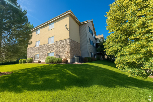 View of side of property featuring a lawn, stone siding, and stucco siding