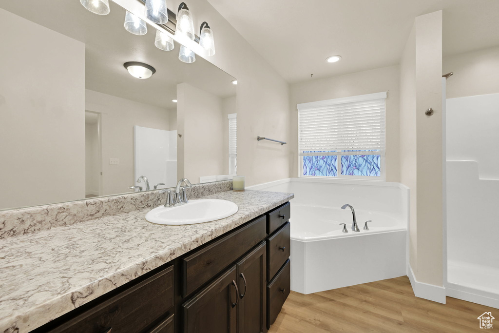 Bathroom featuring a garden tub, wood finished floors, walk in shower, vanity, and recessed lighting