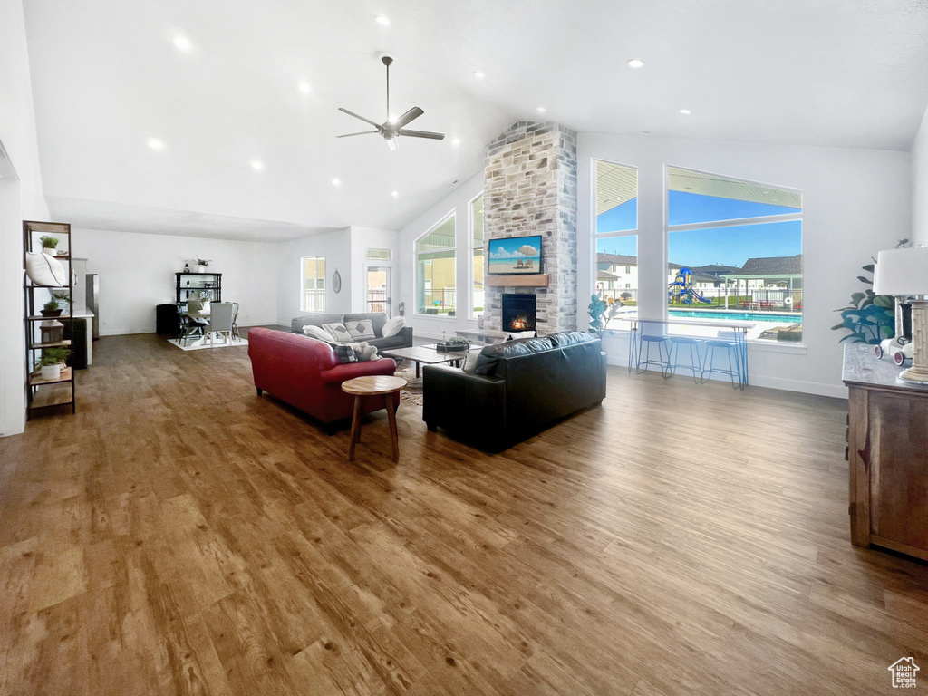 Living area featuring ceiling fan, high vaulted ceiling, a stone fireplace, wood finished floors, and baseboards