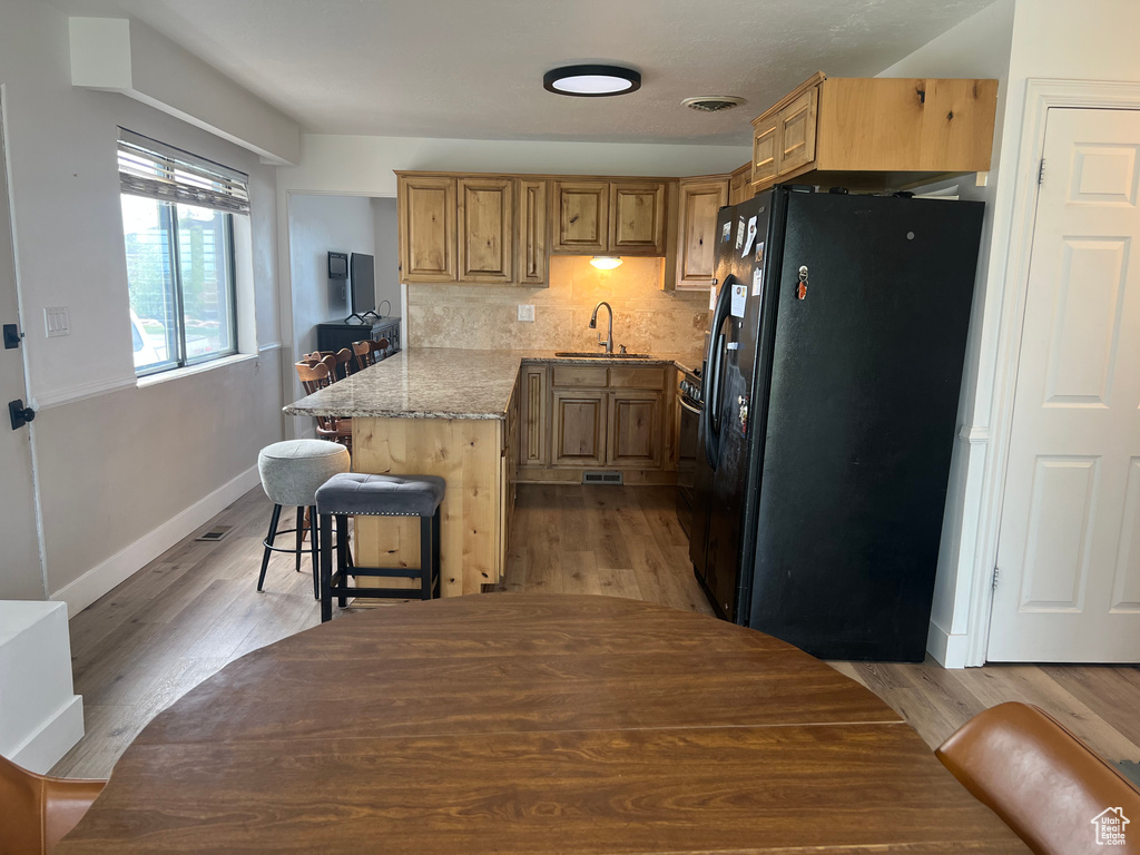 Kitchen with a sink, a peninsula, a kitchen breakfast bar, black fridge, and baseboards