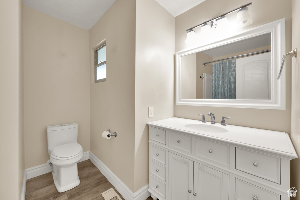 Bathroom featuring toilet, visible vents, baseboards, wood finished floors, and vanity