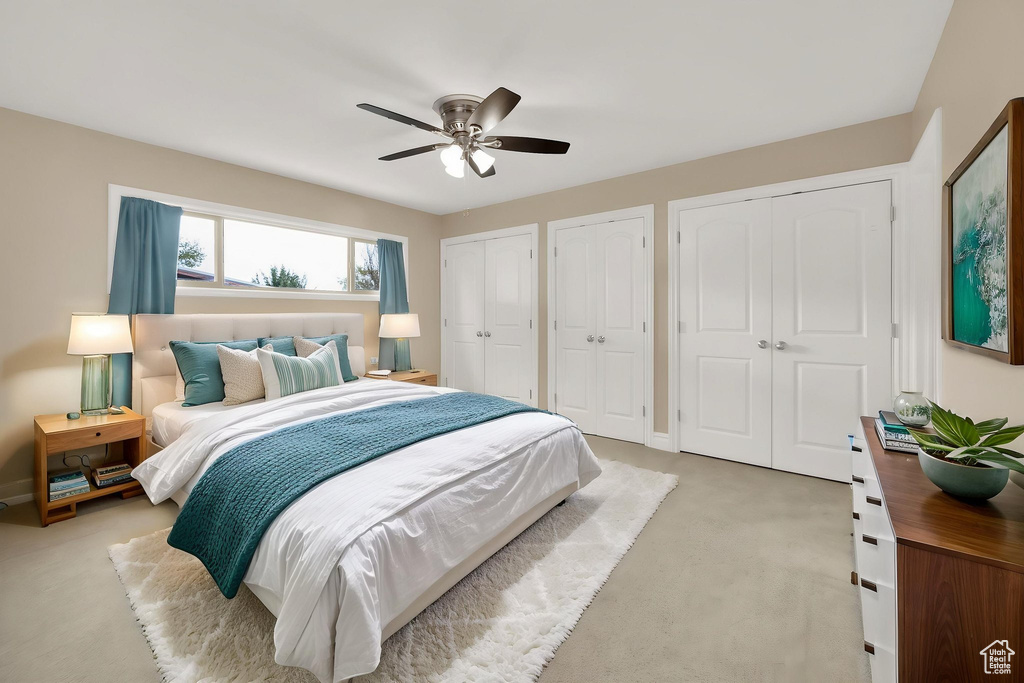 Bedroom with light colored carpet, ceiling fan, baseboards, and multiple closets