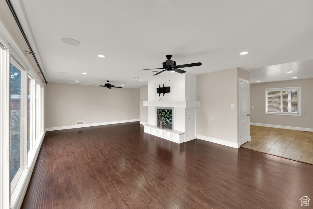 Unfurnished living room with a fireplace with raised hearth, wood finished floors, visible vents, baseboards, and ceiling fan
