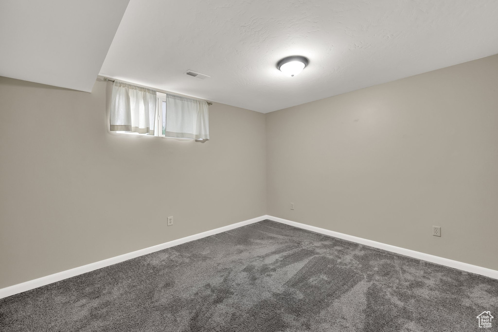 Unfurnished room with dark carpet, visible vents, and baseboards