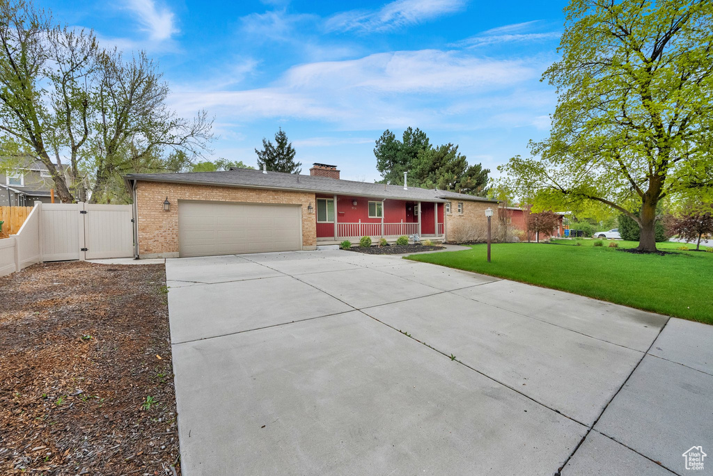 Single story home featuring a gate, a front lawn, concrete driveway, an attached garage, and covered porch
