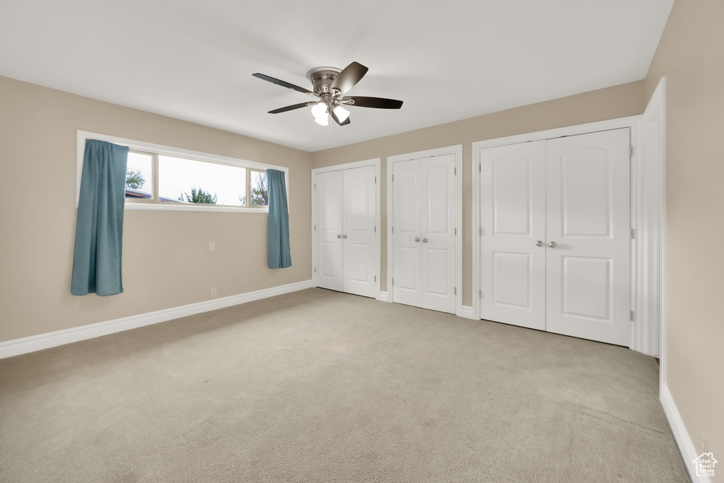Unfurnished bedroom featuring multiple closets, baseboards, carpet floors, and ceiling fan