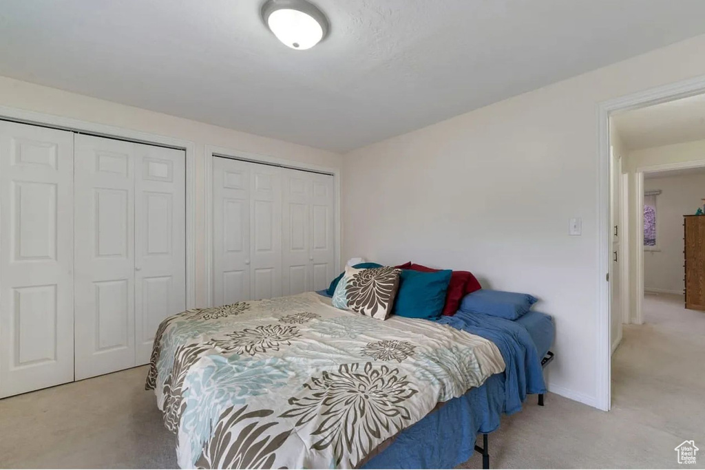 Bedroom with baseboards, two closets, and light colored carpet