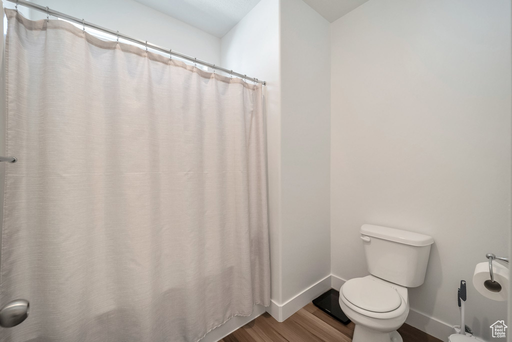 Bathroom featuring wood finished floors, toilet, and baseboards
