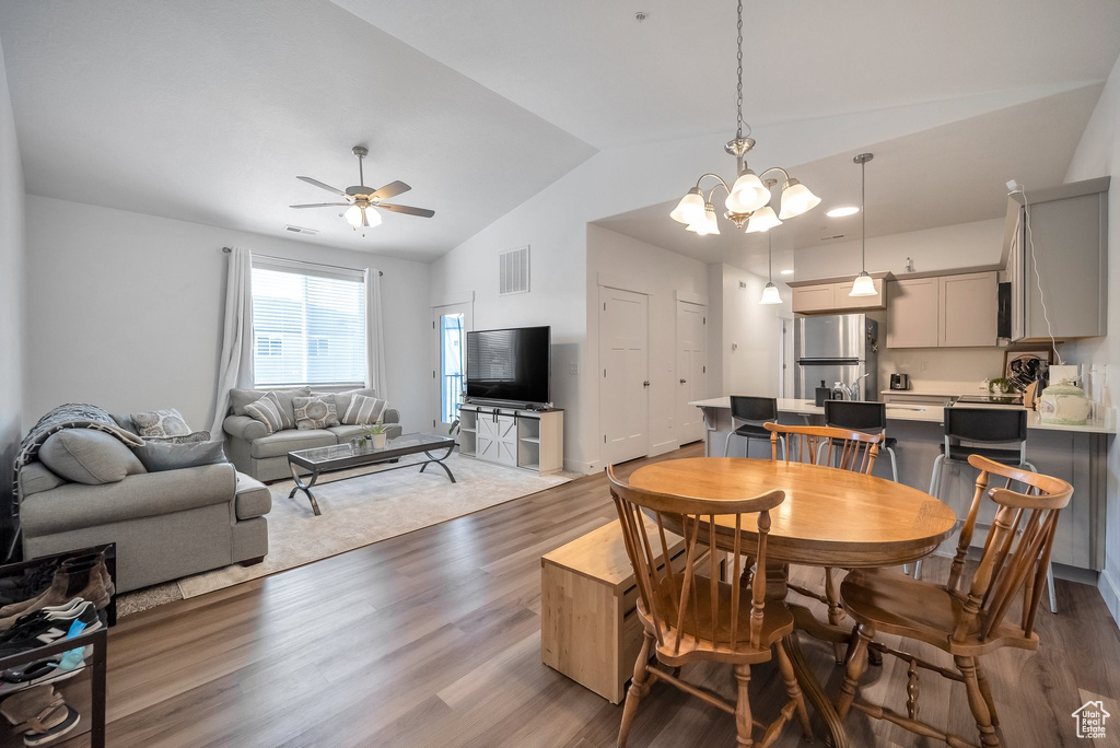 Dining area featuring lofted ceiling, wood finished floors, visible vents, and ceiling fan with notable chandelier