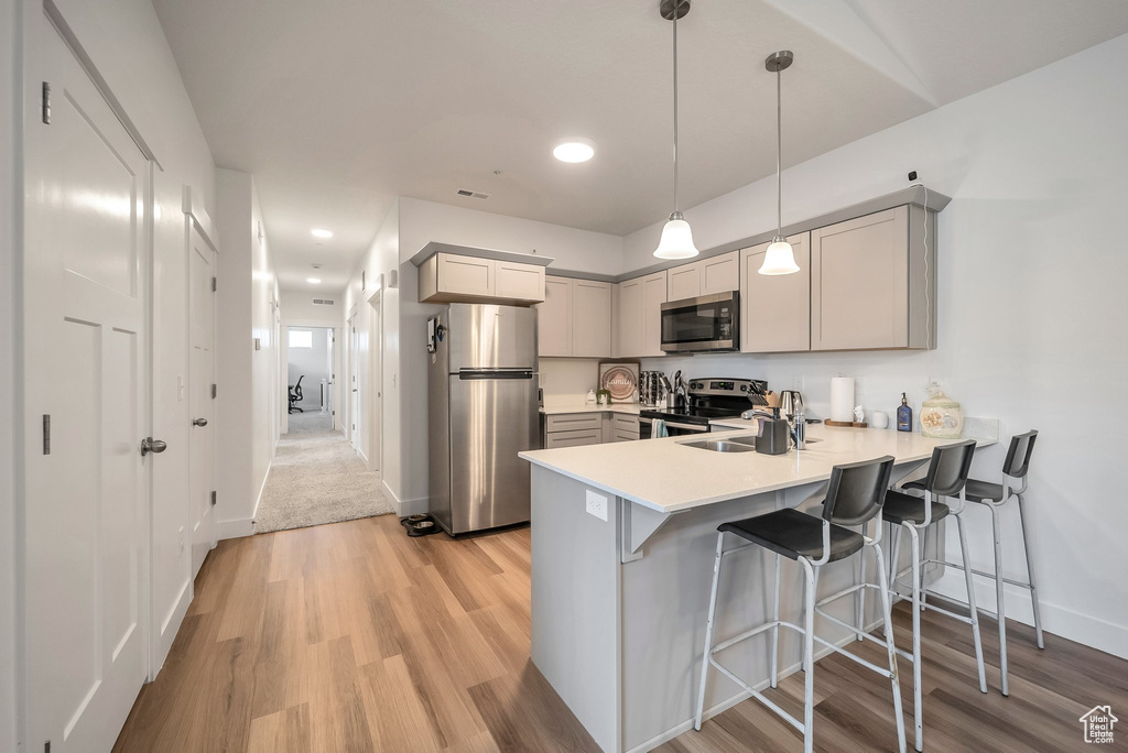 Kitchen with a peninsula, baseboards, light wood-style floors, light countertops, and appliances with stainless steel finishes
