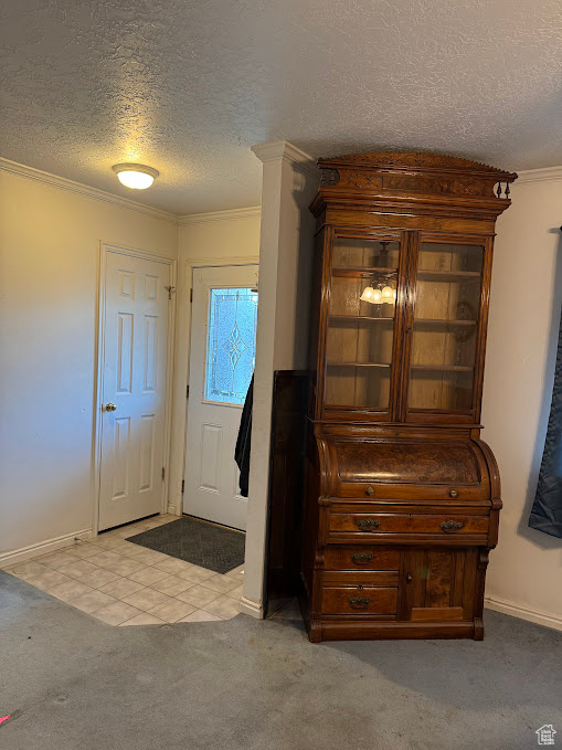 Carpeted entrance foyer featuring a textured ceiling, ornamental molding, and baseboards