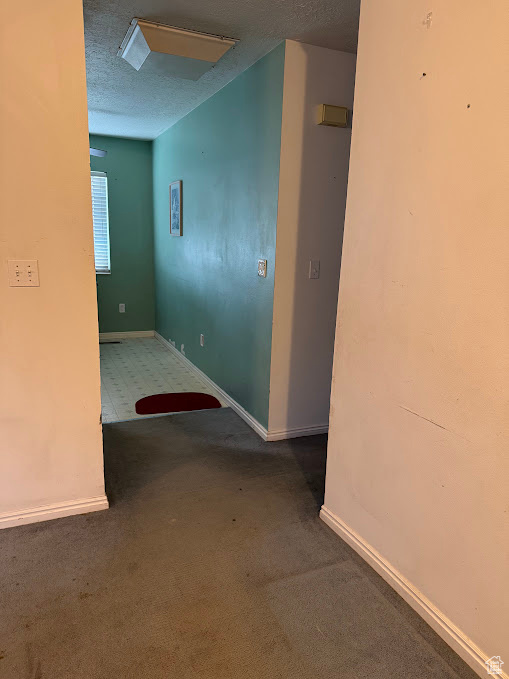 Hallway featuring carpet, a textured ceiling, and baseboards