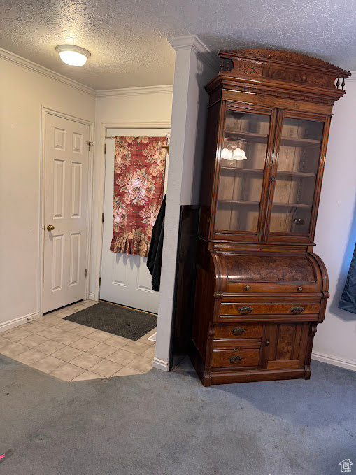 Carpeted entrance foyer featuring a textured ceiling, ornamental molding, baseboards, and tile patterned flooring