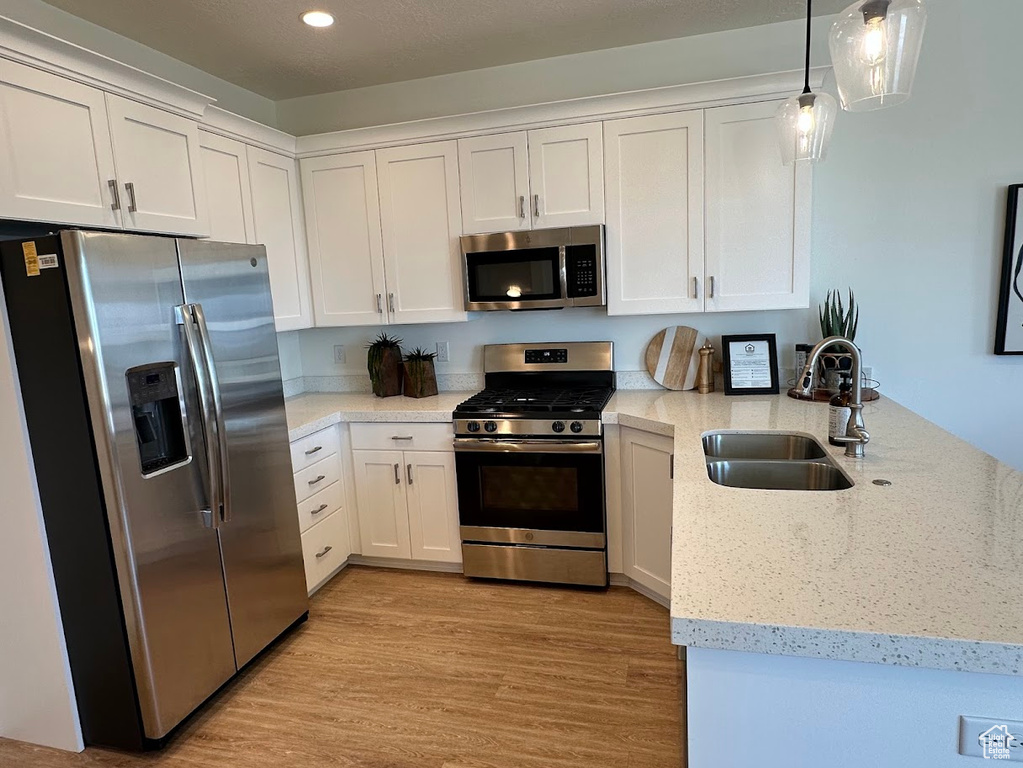 Kitchen with a peninsula, white cabinetry, stainless steel appliances, and a sink