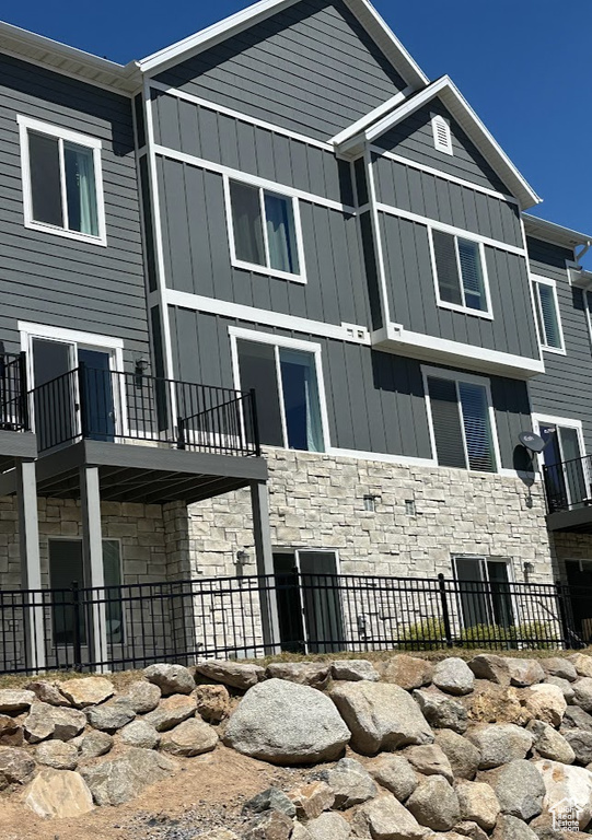 Rear view of property featuring stone siding, fence, board and batten siding, and a balcony