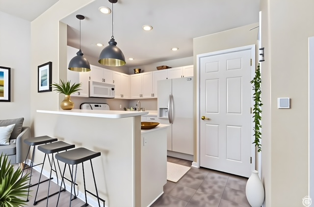 Kitchen with white appliances, a kitchen breakfast bar, a peninsula, recessed lighting, and white cabinetry