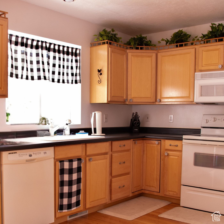 Kitchen with white appliances, light wood-style floors, and dark countertops