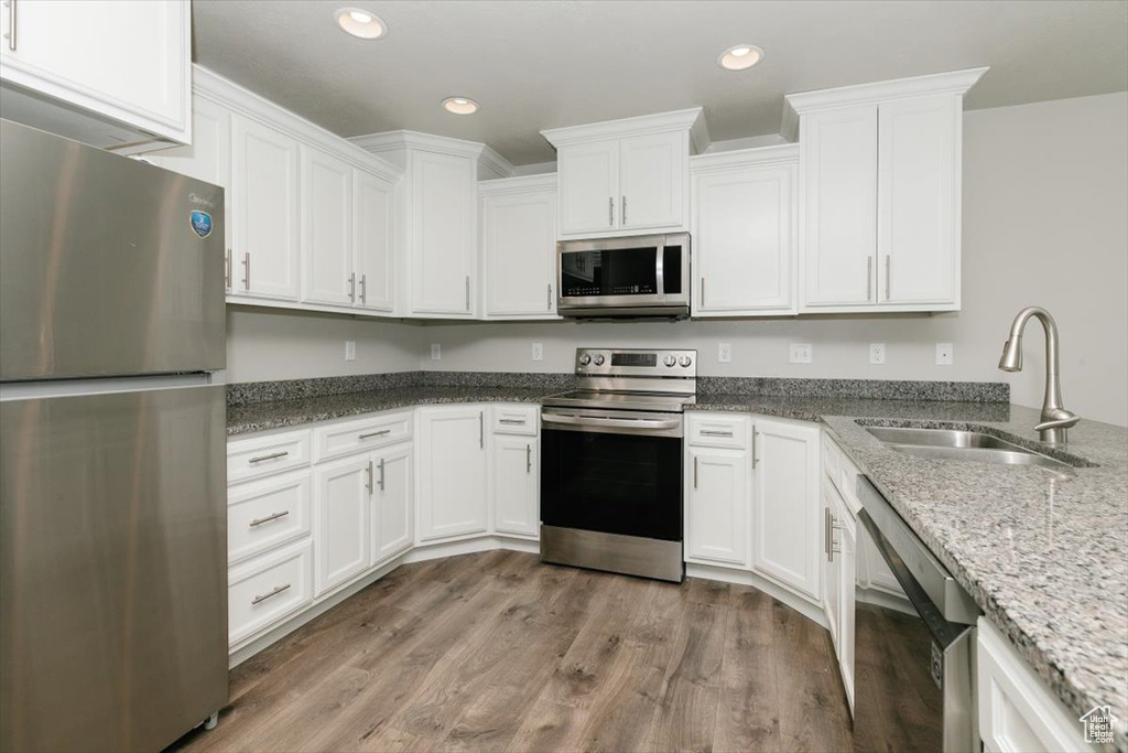 Kitchen with appliances with stainless steel finishes, a sink, white cabinetry, light stone counters, and recessed lighting