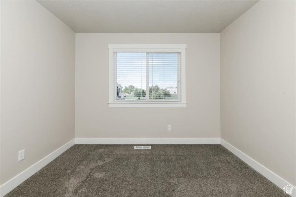 Empty room featuring dark carpet and baseboards