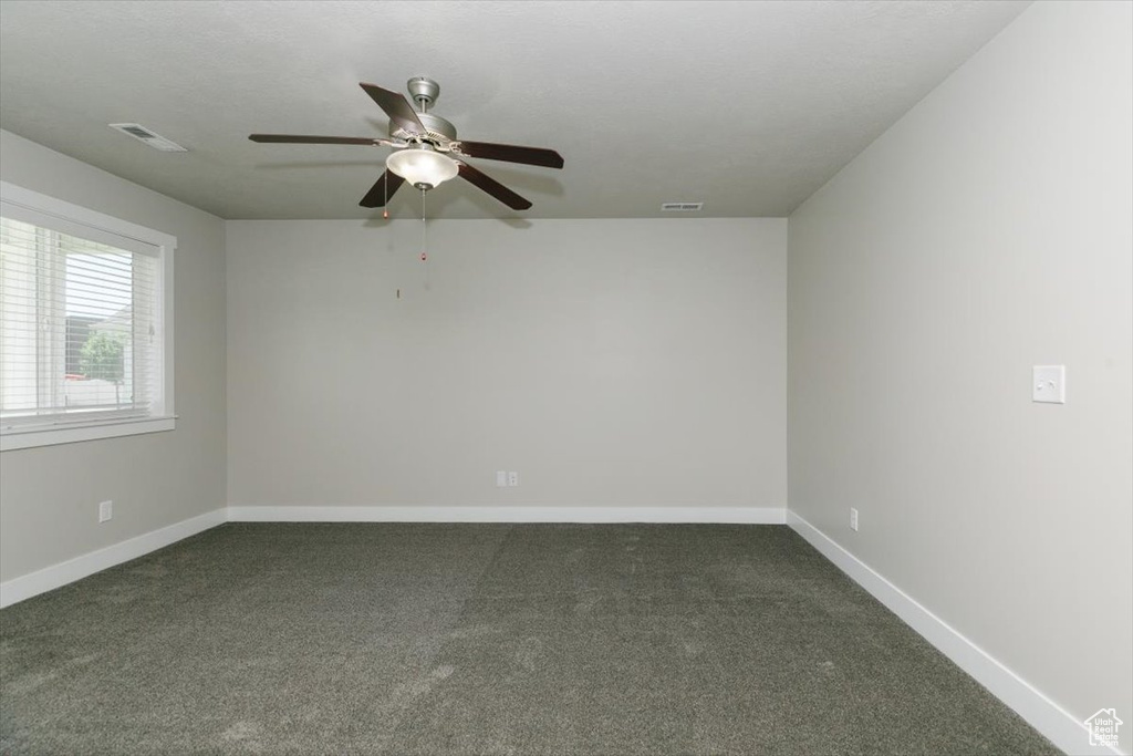 Spare room with ceiling fan, dark colored carpet, and baseboards