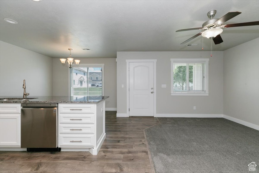 Kitchen featuring stainless steel dishwasher, a sink, a chandelier, white cabinetry, and baseboards