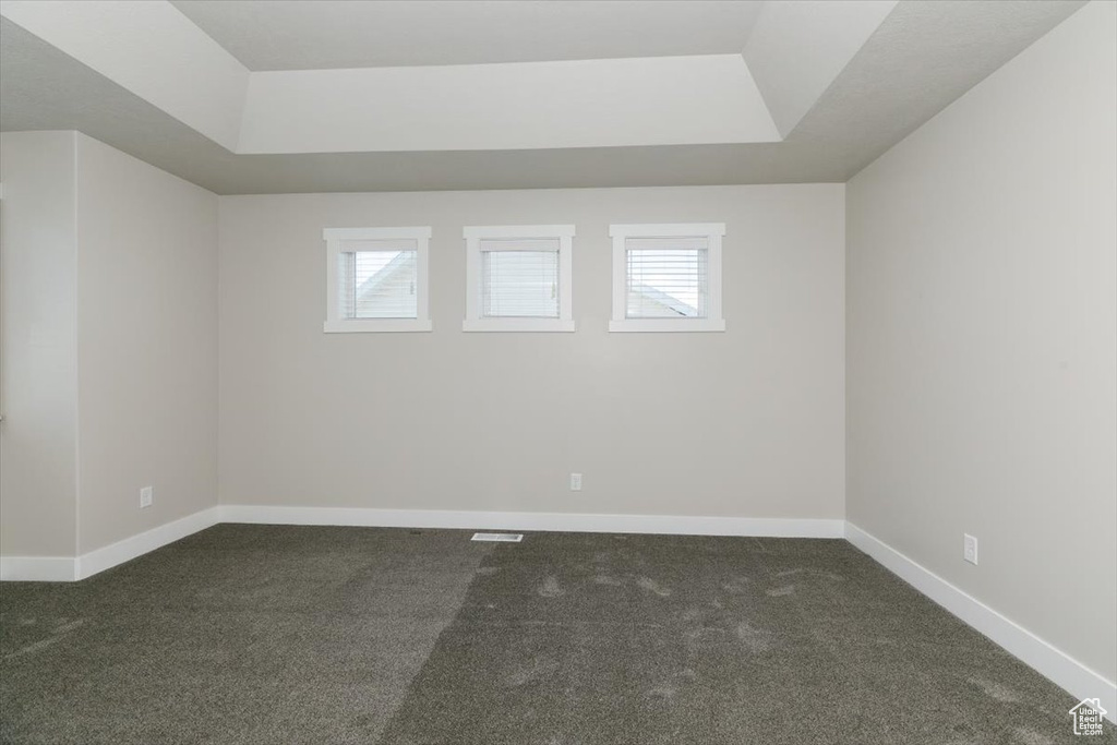 Spare room with dark colored carpet, a raised ceiling, and baseboards
