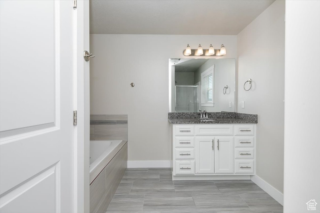 Full bathroom featuring vanity, a bath, baseboards, and a shower with shower door