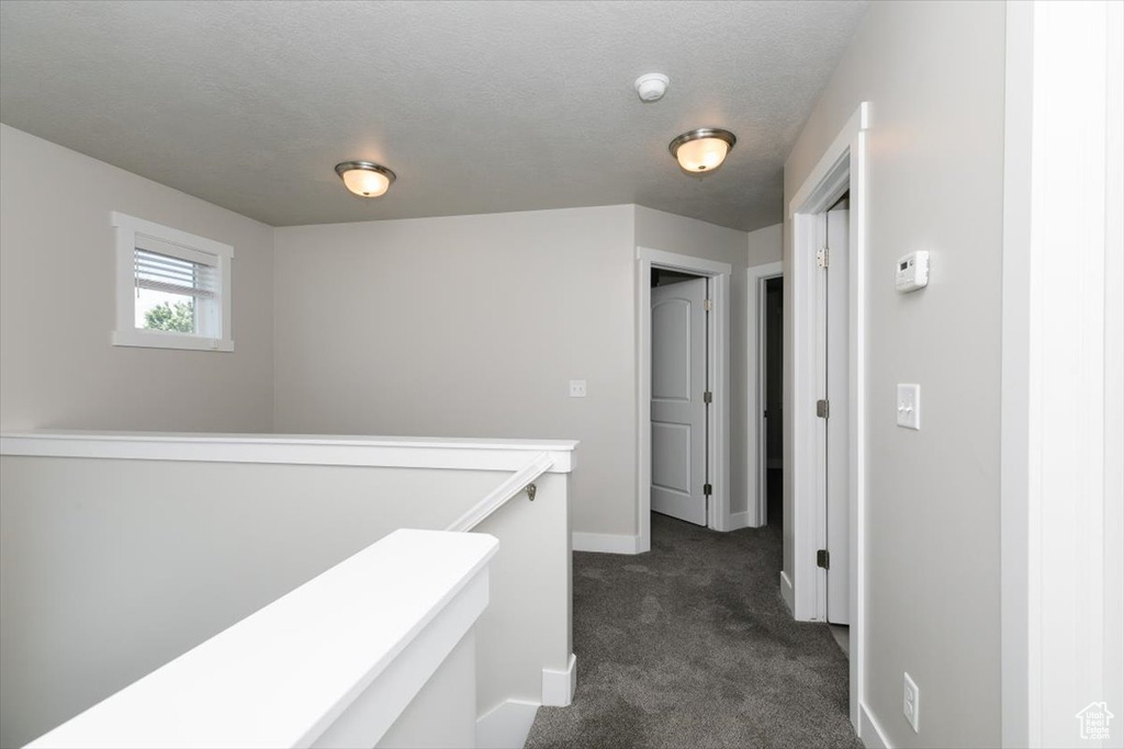 Hallway featuring dark colored carpet, an upstairs landing, and baseboards