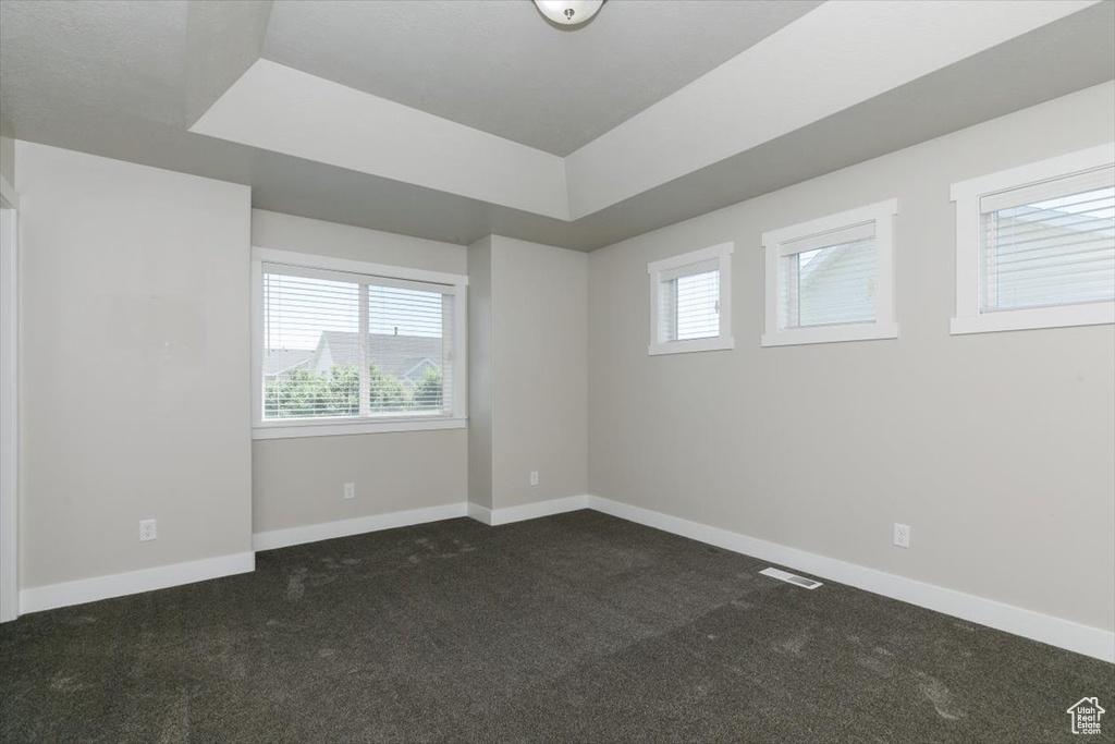 Spare room featuring dark colored carpet, baseboards, and a raised ceiling