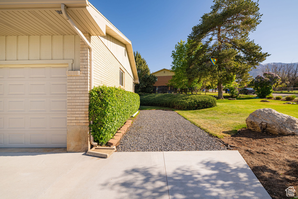 View of property exterior featuring a garage, brick siding, board and batten siding, a lawn, and a mountain view