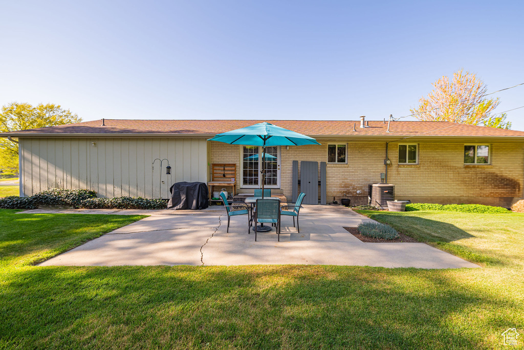 Rear view of property with a lawn, a patio, central AC unit, and brick siding