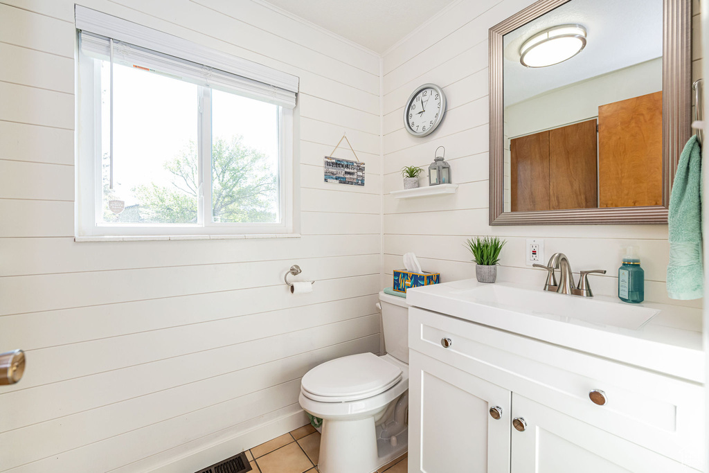 Bathroom featuring vanity, toilet, tile patterned floors, wood walls, and visible vents