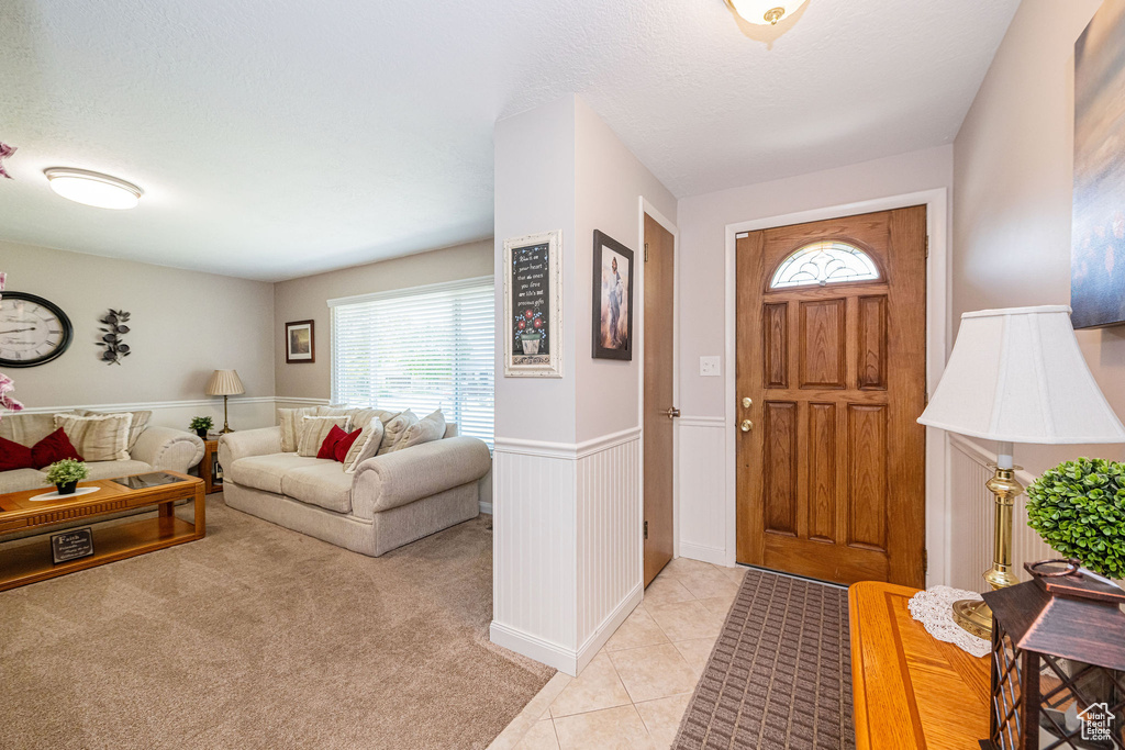 Entryway with a textured ceiling, light tile patterned floors, and a wainscoted wall