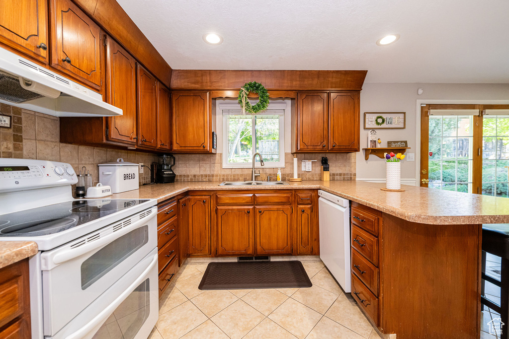 Kitchen with a sink, white appliances, brown cabinetry, a peninsula, and under cabinet range hood