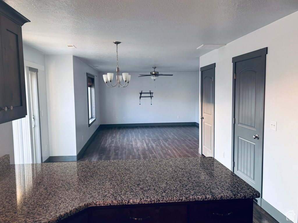 Empty room featuring dark wood-style flooring, a chandelier, ceiling fan, baseboards, and a textured ceiling