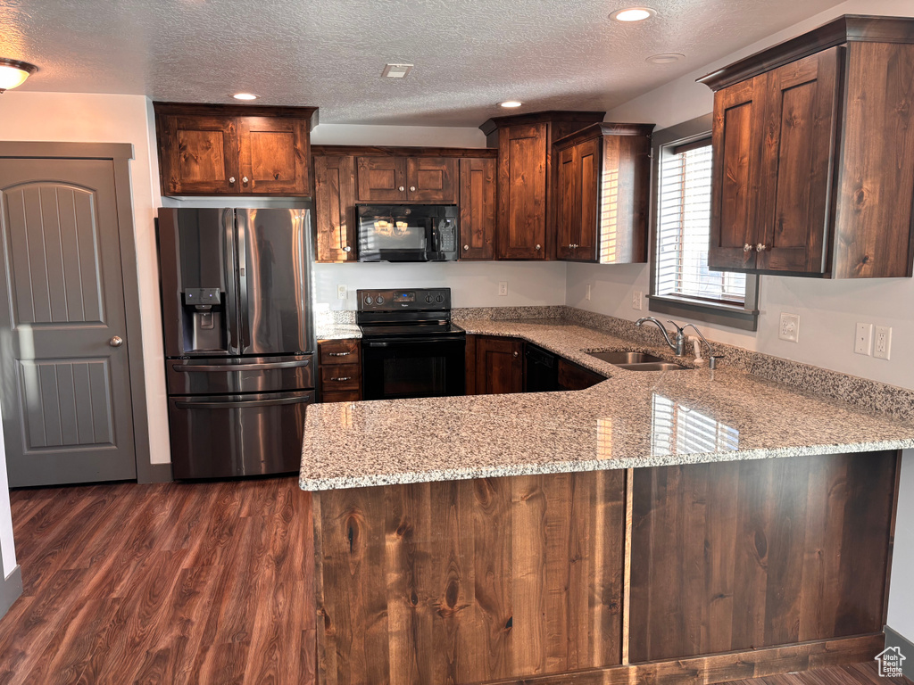 Kitchen featuring black appliances, a sink, a peninsula, a textured ceiling, and light stone counters