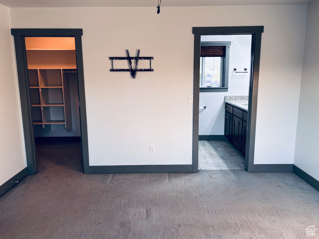 Unfurnished bedroom featuring carpet, baseboards, a spacious closet, and ensuite bath