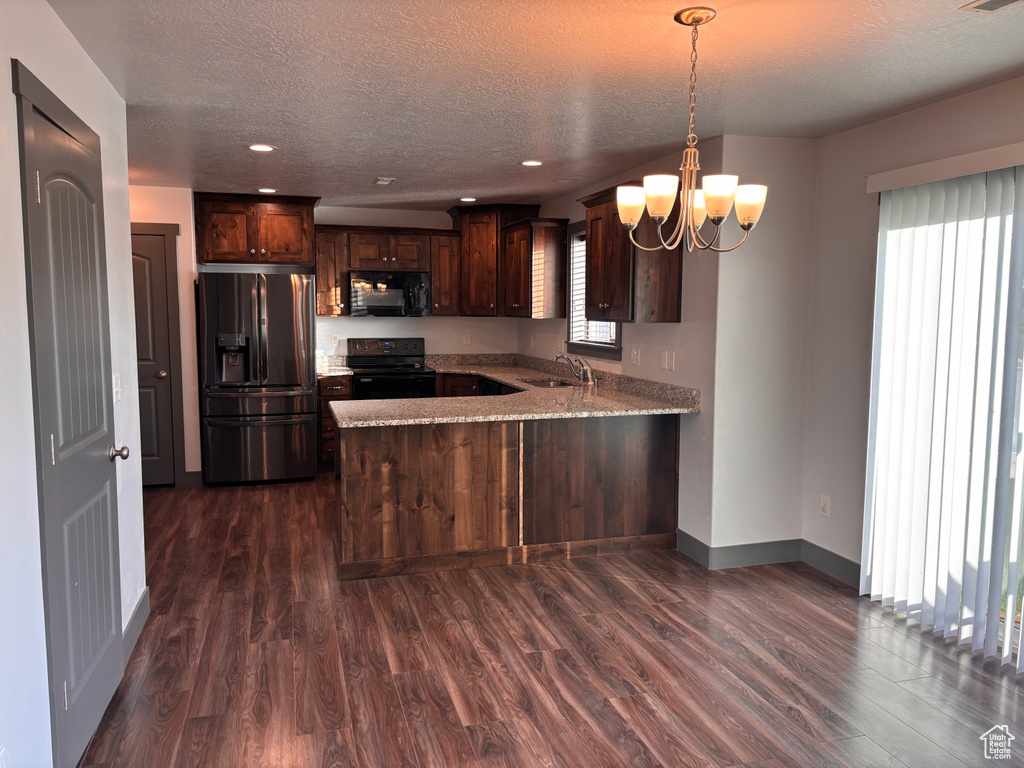 Kitchen with black appliances, a sink, a peninsula, dark brown cabinets, and dark wood finished floors