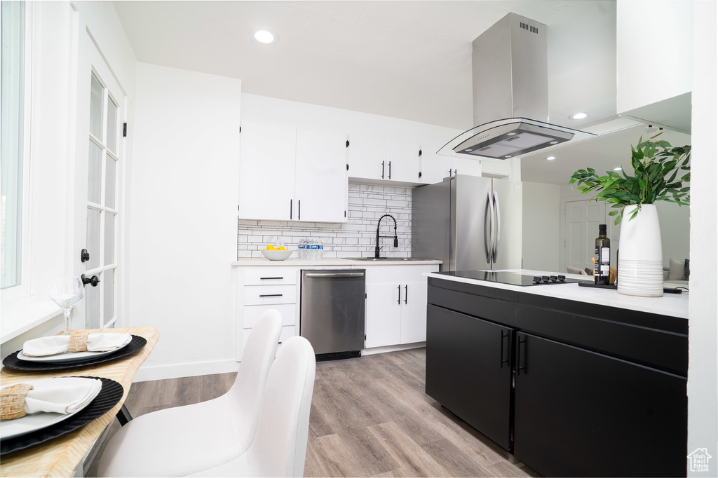 Kitchen with island exhaust hood, light countertops, a sink, appliances with stainless steel finishes, and white cabinetry