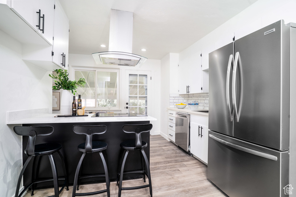 Kitchen with white cabinets, stainless steel appliances, a peninsula, island range hood, and light countertops