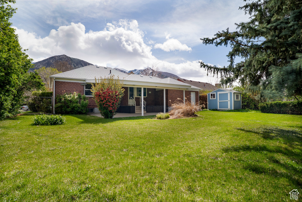 Back of property with a storage shed, a yard, a patio area, an outdoor structure, and brick siding