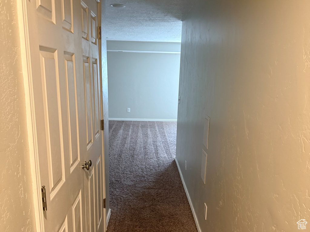 Hallway with carpet floors, baseboards, and a textured wall