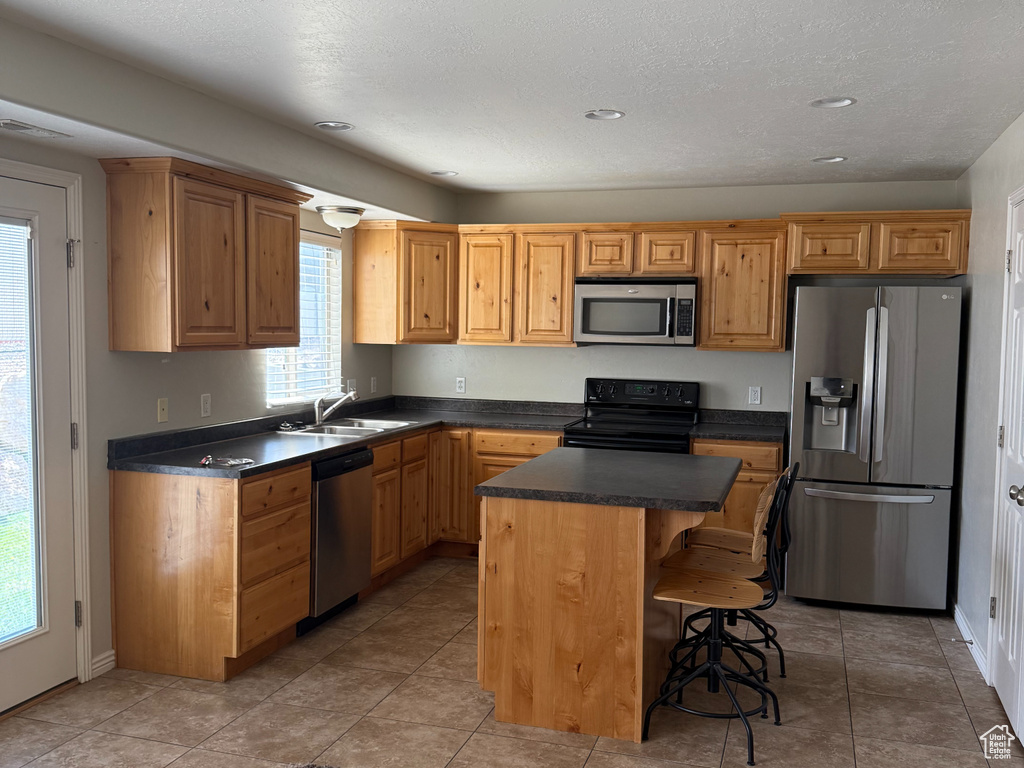 Kitchen with stainless steel appliances, dark countertops, a sink, a kitchen island, and a textured ceiling