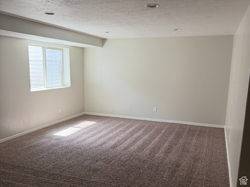 Empty room with carpet, a textured ceiling, and baseboards