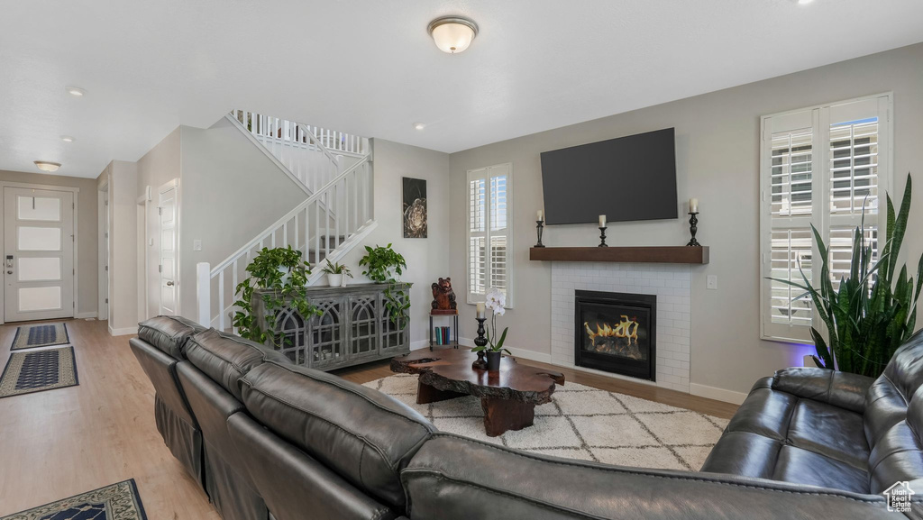 Living room featuring stairs, light wood-type flooring, a glass covered fireplace, baseboards, and recessed lighting