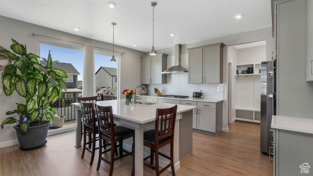 Kitchen with wall chimney exhaust hood, gray cabinetry, a sink, appliances with stainless steel finishes, and light wood-style flooring