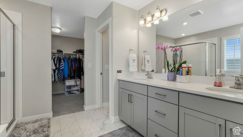 Full bath featuring a shower stall, double vanity, a spacious closet, marble look tile flooring, and baseboards