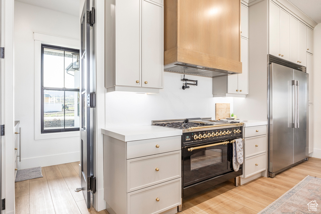 Kitchen with high end appliances, light wood-style floors, light countertops, premium range hood, and baseboards