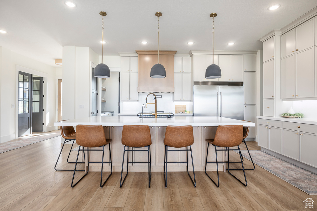 Kitchen featuring light wood finished floors, built in fridge, light countertops, and custom exhaust hood