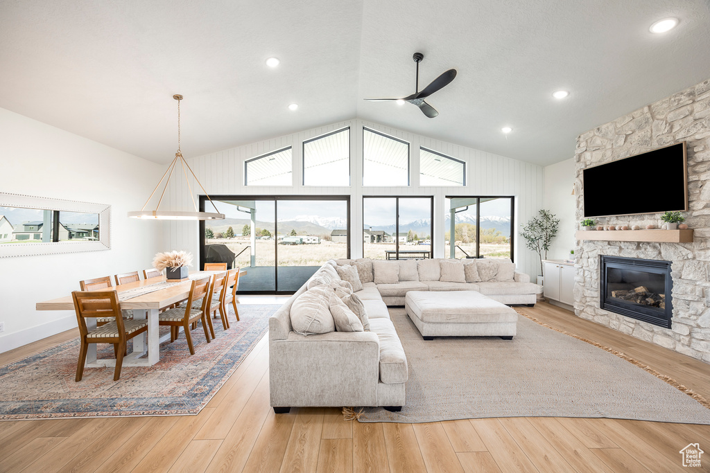 Living room featuring lofted ceiling, wood finished floors, a stone fireplace, and ceiling fan